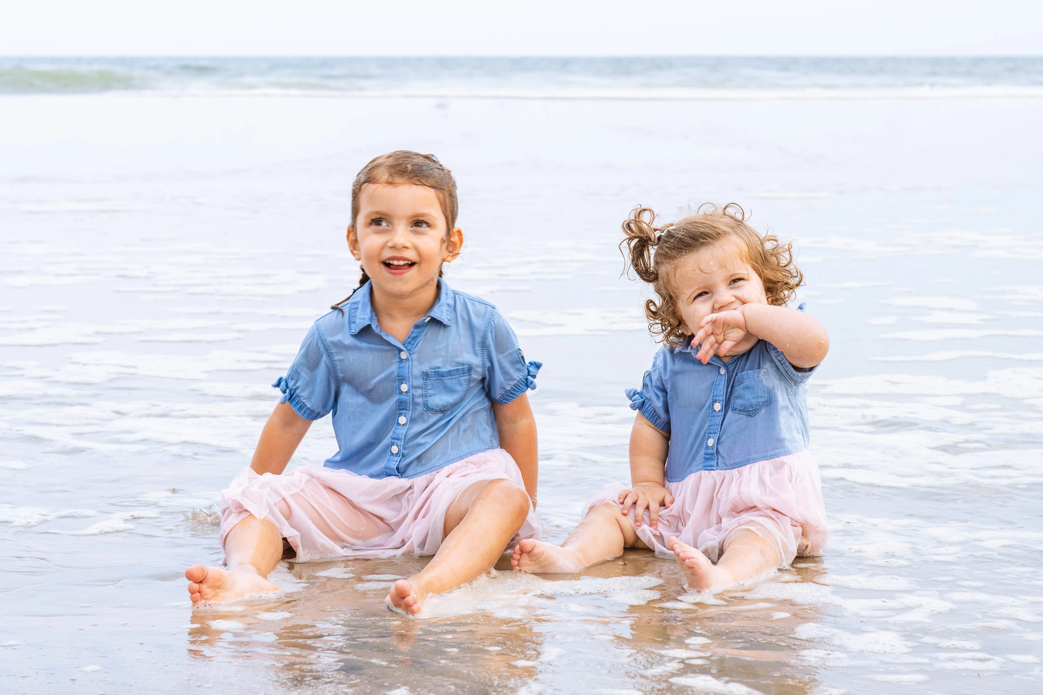 two young girls sitting at the water's edge on the beach