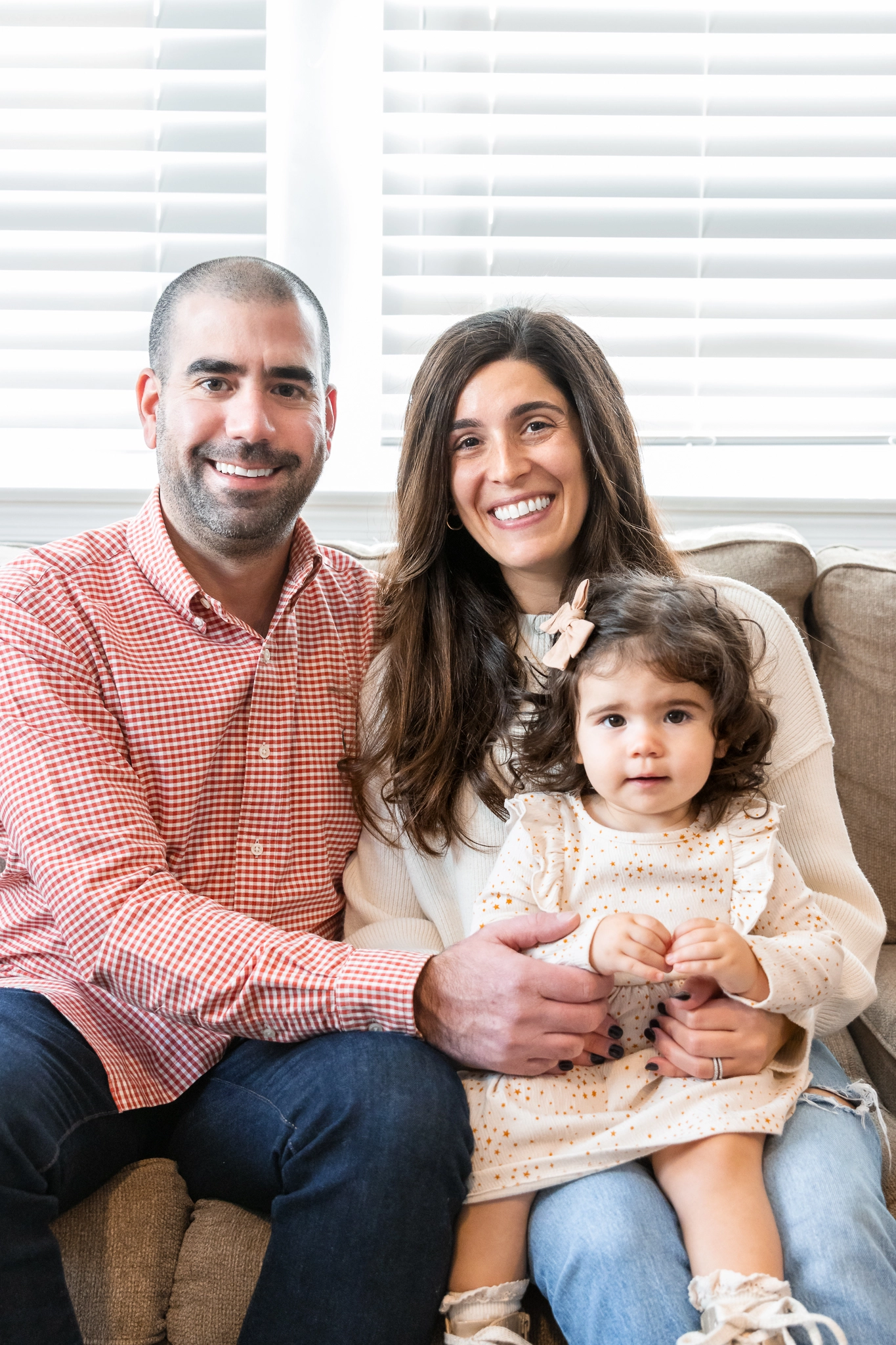 A mom, dad and daughter sitting on their couch smiling for a family portrait